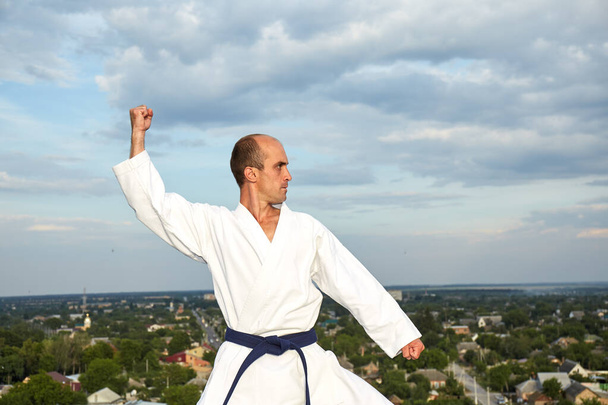 Sportowiec z niebieskim pasem treningowym formalne ćwiczenia karate na tle miasta - Zdjęcie, obraz