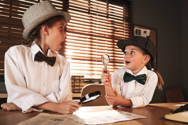 Cute little detectives exploring fingerprints with magnifying glasses at table in office - Zdjęcie, obraz