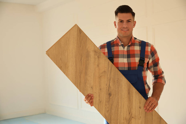 Professional worker with wooden board indoors. Installing of parquet flooring - Foto, Imagem