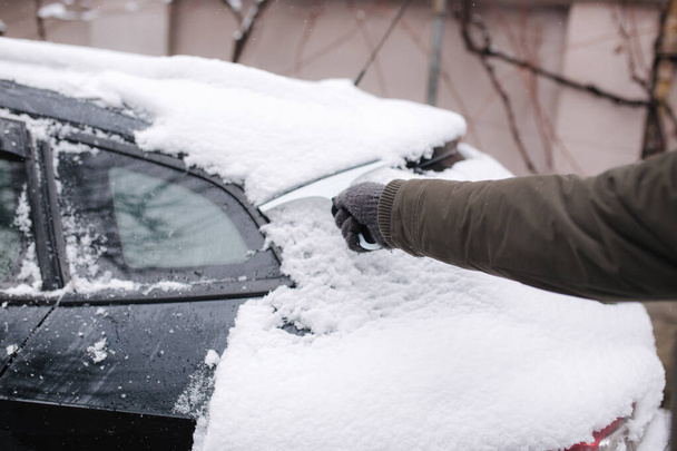 Il primo piano dell'uomo sta pulendo la finestra innevata su un'auto con un raschietto di neve. Concentrati sul raschietto. Fredda mattina nevosa e gelida. Auto nera - Foto, immagini
