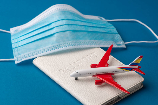 Close-up on medical face mask, passport and airplane toy on blue background - Fotó, kép
