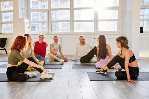 group of young people sitting on the floor having rest after dance of yoga - 写真・画像