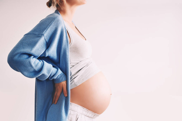 Schöne schwangere Frau umarmt ihren Bauch vor weißem Hintergrund. Werdende Mütter warten während der Schwangerschaft auf die Geburt ihres Kindes. Konzept der Müttergesundheit, Arztbesuche und gynäkologische Untersuchungen. - Foto, Bild