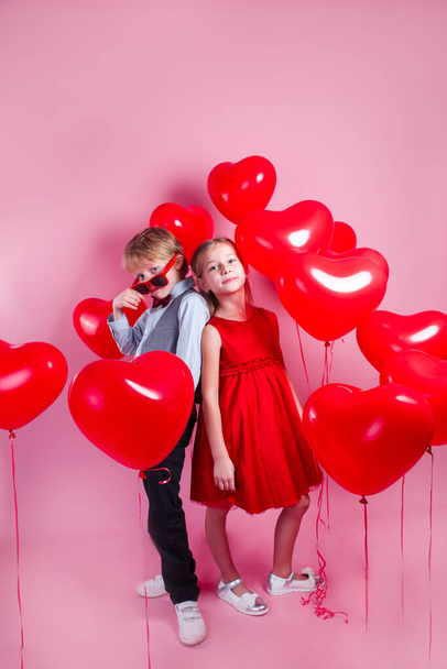 Valentines day photo. Children with red heart balloons on a pink background - Foto, afbeelding