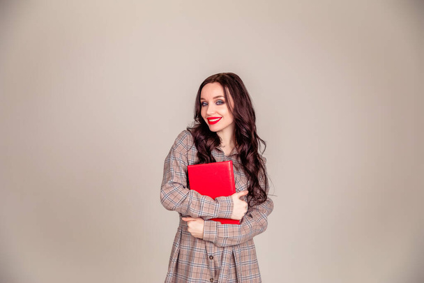 a beautiful young girl with red lips holds a red notebook in her hands. student. businesswoman on isolated gray background. the concept of education. Copy space - Photo, image