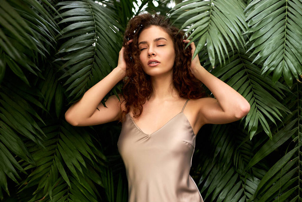 attractive curly young woman in silk dress poses in botanical garden - Photo, Image