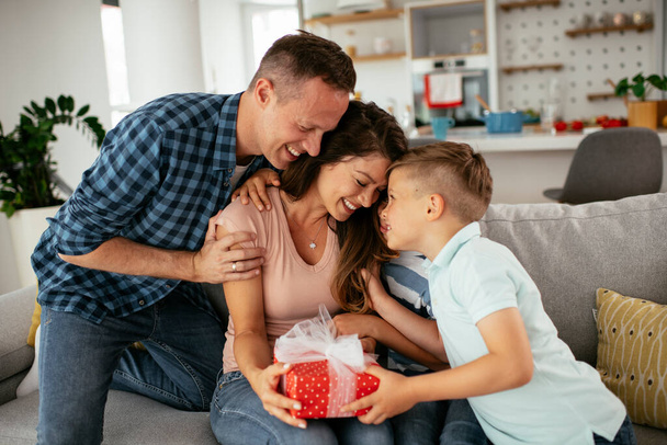 Vater mit zwei kleinen Söhnen machen ihrer Mutter ein Geschenk. Mutter überrascht über Geschenk von Söhnen und Ehemann - Foto, Bild