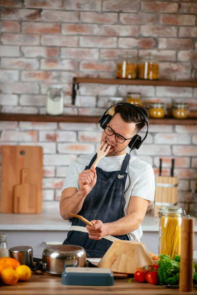 Homme heureux dans les écouteurs écouter de la musique et danser tout en cuisinant dans la cuisine. - Photo, image