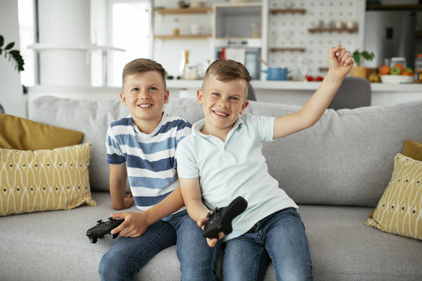Jonge broers hebben plezier tijdens het spelen van videospelletjes in de woonkamer - Foto, afbeelding
