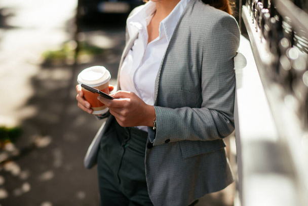 Young and beautiful businesswoman using phone on coffee break while walking on the street - 写真・画像