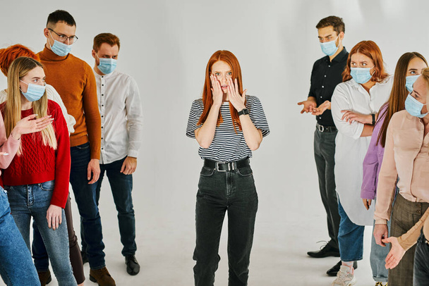 group of healthy people in medical masks avoid contact with an infected redhead woman standing in center - Foto, Imagen