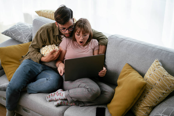Fiatal pár filmet néz laptopon. Szerető pár, akik otthon élvezik. - Fotó, kép