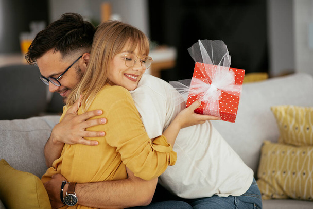 Boyfriend surprising his girlfriend with a gift. Young man giving gift box to his wife - Foto, Imagen