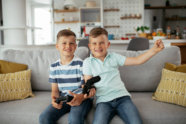 Young brothers having fun while playing video games in living room - Foto, afbeelding