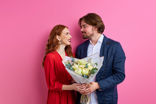 affectionate caucasian man offering his partner roses on pink background - Fotó, kép