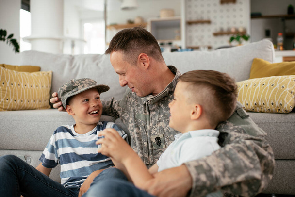 Szczęśliwy żołnierz siedzący na podłodze z rodziną. Żołnierz korzystających w domu z dziećmi. - Zdjęcie, obraz