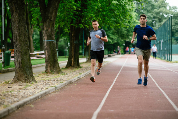 Young men training on a race track. Two young friends running on athletics track - Photo, Image