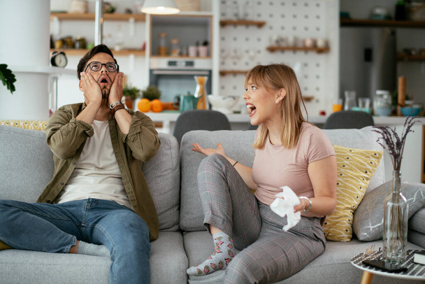 Boyfriend and girlfriend are arguing on the couch. Angry woman is yelling at her boyfriend. - Fotó, kép