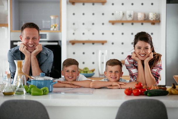 Mother and father making breakfast with sons. Young family preparing delicious food in kitchen and having fun - Photo, Image