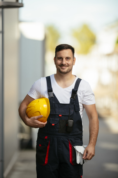 Портрет улыбающегося рабочего с желтым шлемом в руке - Фото, изображение