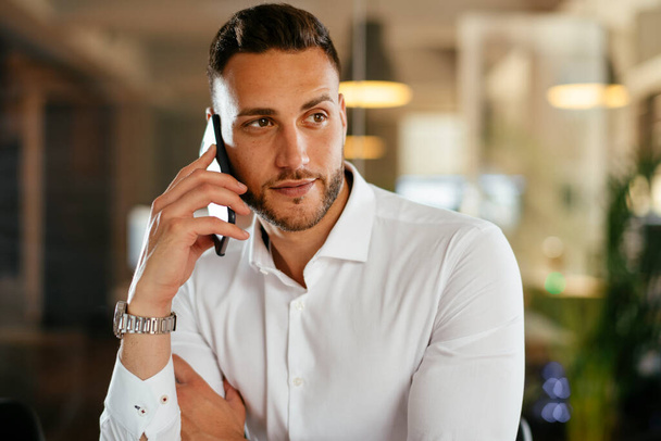 Businessman discussing work on phone. Young businessman talking on the phone at the office. - 写真・画像