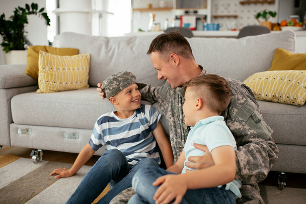 Ευτυχισμένος στρατιώτης που κάθεται στο πάτωμα με την οικογένειά του. Στρατιώτης απολαμβάνει στο σπίτι με τα παιδιά. - Φωτογραφία, εικόνα