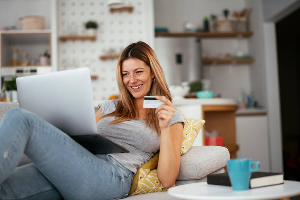 Young woman using her credit card and laptop at home. Beautiful woman buying online. - Fotografie, Obrázek