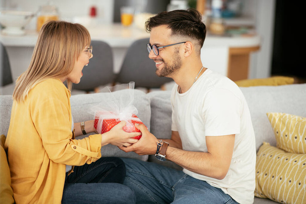 Boyfriend surprising his girlfriend with a gift. Young man giving gift box to his wife - Foto, Bild