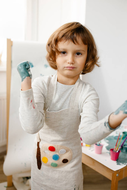 Child girl painting her hand with paint and paintbrush. Finger painting or art therapy for children. Fun activities for toddlers. - Photo, image