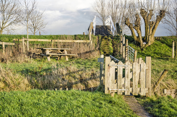 Facilities for hikers in the polder near Maasland, The Netherlands: a bench and picknick table, steps, a narrow bridge, a footpath and a door in a fence - Photo, Image