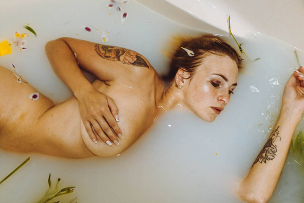 Attractive nude girl enjoying a bath with milk and yellow flowers and leaves. Spa body care. Tenderness, beauty and care. Time for rest and relaxation. - Photo, image