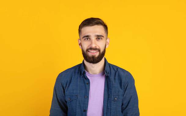 Ξέγνοιαστος νεαρός κοιτάζοντας κάμερα και χαμογελώντας πάνω από πορτοκαλί φόντο στούντιο, πανόραμα - Φωτογραφία, εικόνα
