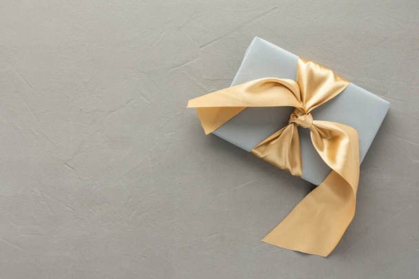 Gray gift box with golden bow on a gray concrete background, birthday or valentine concept, top view, copy space - Photo, Image