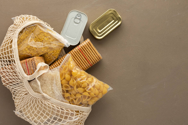 Home food supplies, necessary food for the period of quarantine and isolation, the concept of stay at home, eco bag with assorted pasta, rice and bulgur, cookies and canned food,top view - Photo, Image