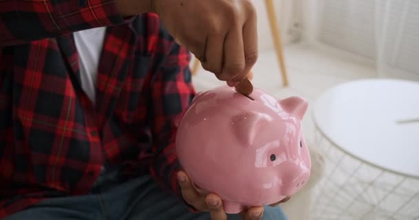 Mann steckt Münze in Sparschwein und schüttelt sich - Filmmaterial, Video