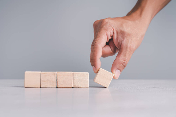 Businessman wearing a blue shirt, arranging the empty wooden blocks with his hands. Which is placed on a white wooden table. Business strategy and action plan. Copy space. - Photo, Image