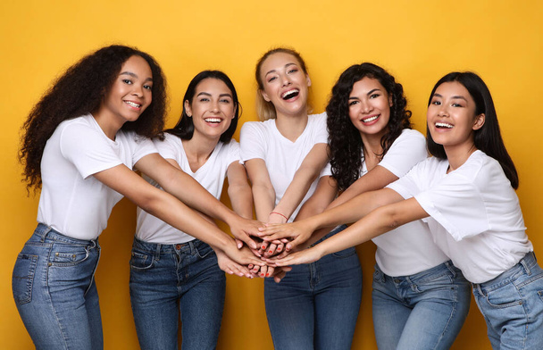 Vijf gelukkig multi-etnische vrouwen houden handen poseren op gele achtergrond - Foto, afbeelding
