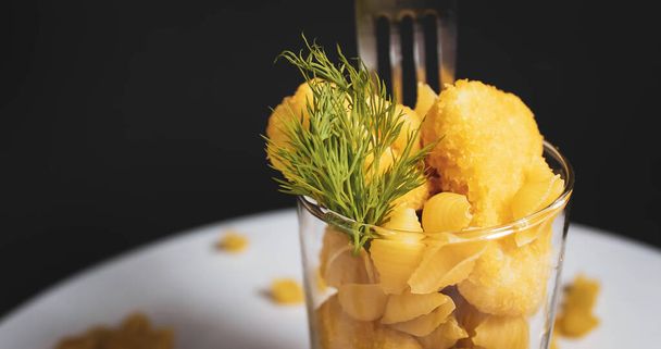 A glass cup with nuggets and pasta, with a drinking straw. Creative still life. Close-up. - Foto, Imagen
