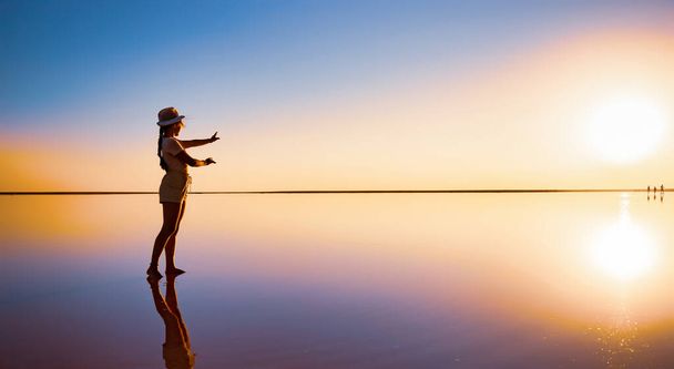 A girl reaches out with her hands to the setting sun on the mirror surface of a salt lake - Foto, afbeelding