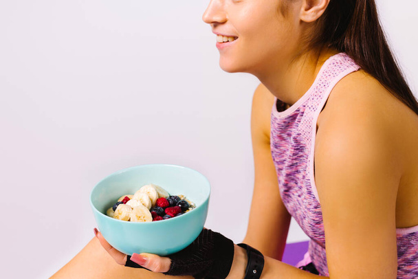 Cropped photo of a sportive girl with a plate of oatmeal and berries. Sport and nutritional detox online blog concept on white background. - Foto, afbeelding