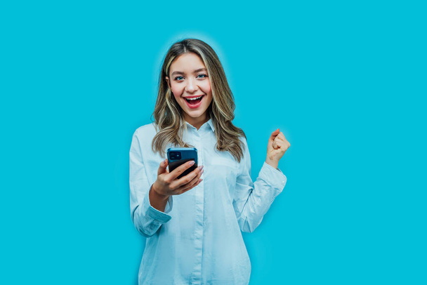 Attractive girl on a blue background with a phone in her hands, she is happy with the purchase she made online. Place for text, online shopping. - Photo, Image