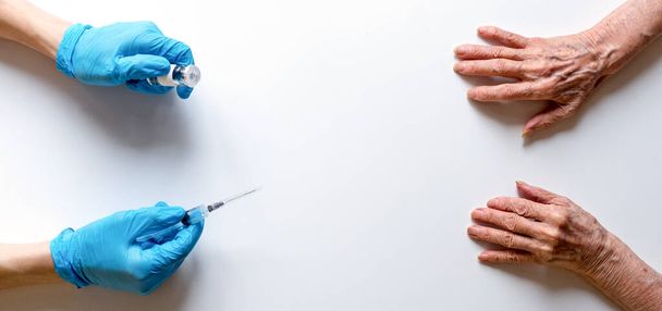 Spritze und Ampulle mit Medikamenten in den Händen eines Arztes in medizinischen Handschuhen auf weißem Hintergrund, die ausgestreckten Hände einer älteren Frau - Foto, Bild