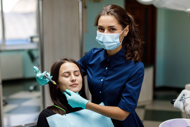 Fiatal nő ül a fogorvosi székben, és a fogorvos gondosan megvizsgálja a beteg fogait. A fogorvos konzultál egy beteggel, aki egy széken ül a klinikán. - Fotó, kép
