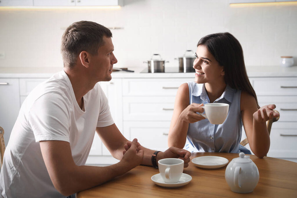 Man and woman talking while drinking tea at table in kitchen - Foto, Bild