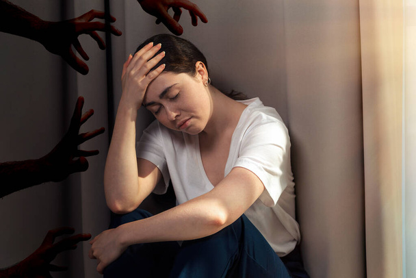 Porträt einer depressiven jungen Frau, die ihren Kopf mit der Hand hält. Dunkle Hände greifen nach der Frau. Das Konzept der häuslichen Gewalt. - Foto, Bild