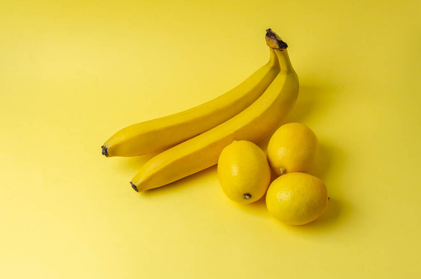 Duas bananas e três limão em um fundo amarelo. Trending Pantone cor do ano 2021 Iluminando. Vista lateral mínima natureza morta. - Foto, Imagem
