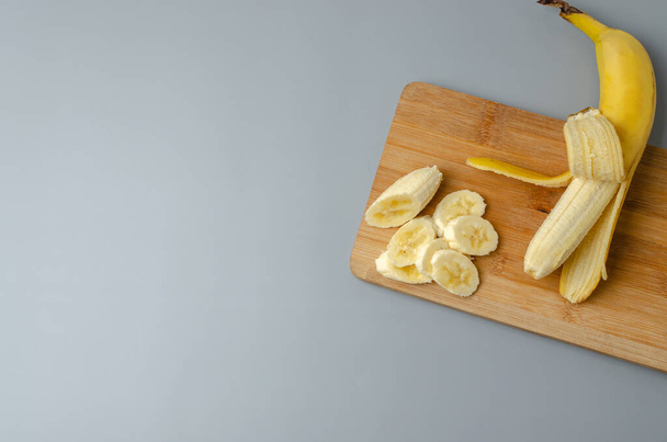 Sliced banana on wood cutting board on a gray background. Trending color Pantone of year 2021 Illuminating and Ultimate gray. Top view minimal still life with copy space. - Foto, immagini