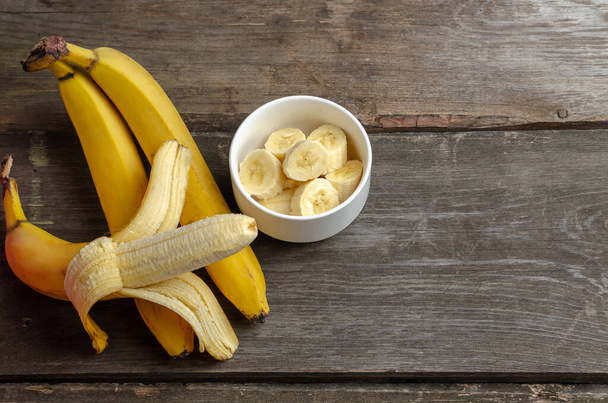 Számos banán és szelet fehér tányérban, rusztikus fa háttéren, fénymásoló felülettel történő főzésre előkészítve. - Fotó, kép