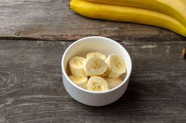 Slices of bananas in a white plate on a rustic wooden background preparing for cooking. - Foto, Imagem