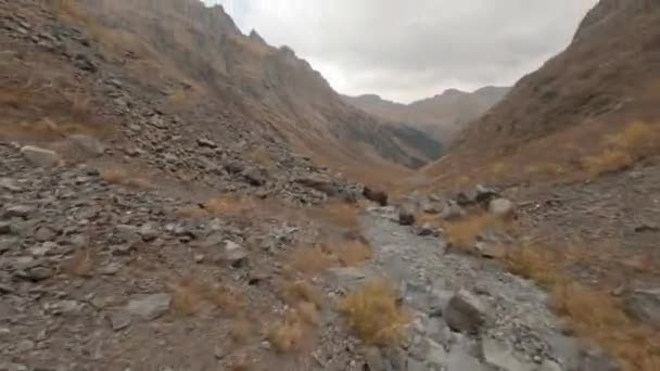 İnsansız hava aracı dağ vadisindeki kayalık nehir yatağını görüyor. Sırt çantalı turistler dağda yürüyüş yapıyor. 4k yükseklikteki kayalar ve kaldırım taşlarıyla fpv drone kuru nehir yatağı üzerinde hava manzarası. - Video, Çekim